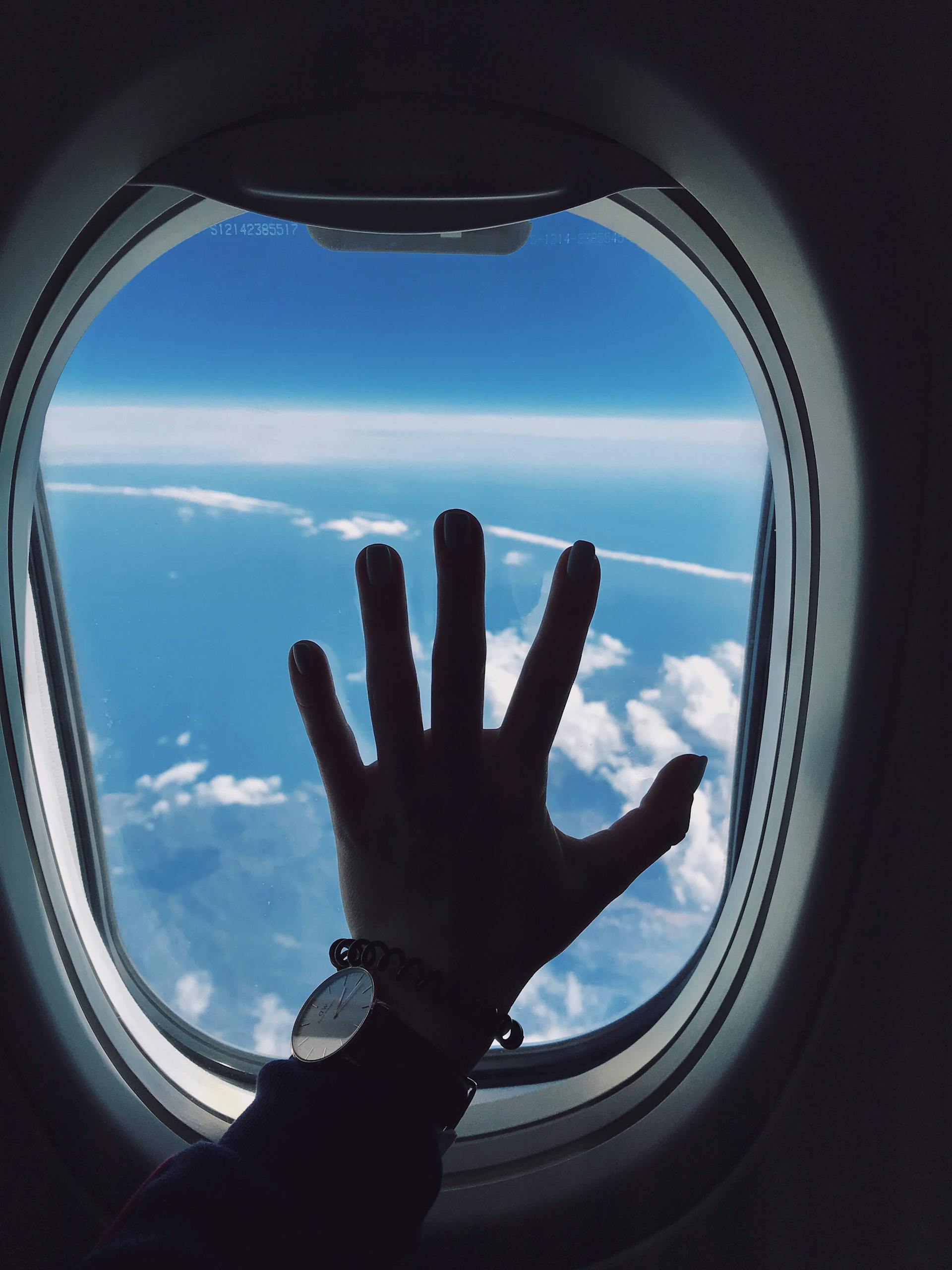 Silhouette of a hand touching an airplane window with a view of clouds and the sky. awardwallet AwardWallet